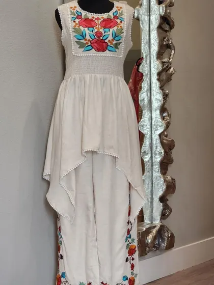 An artistic and chic fusion set. This outfit features an asymmetrical high-low top over pants, both adorned with colorful floral embroidery. It's a wearable work of art.