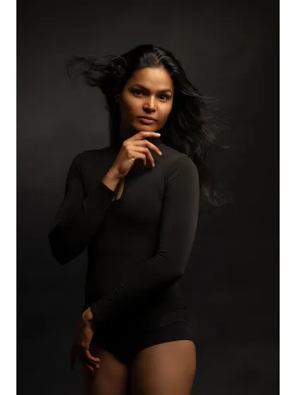 A powerful studio portrait with dramatic lighting. The wind-blown hair and strong pose create a sense of confidence and intensity.