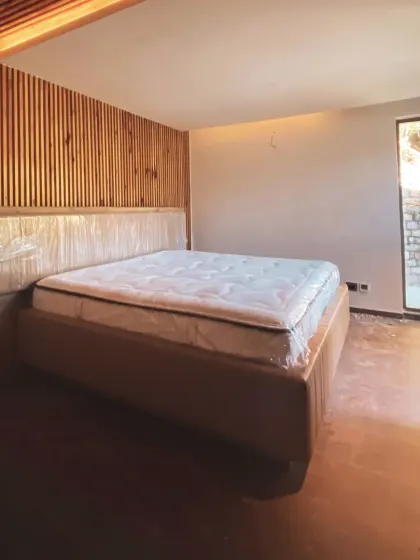 A bedroom in the homestay, featuring a slatted wood accent wall and a large window that directly connects the room to the outdoors. The design prioritizes natural materials and views.