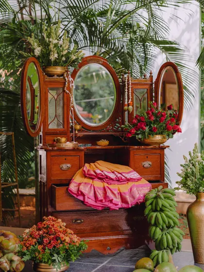 A vintage dressing table used as a decorative prop, draped with a silk saree and adorned with flowers. We use unique furniture pieces to create charming and thematic photo corners.