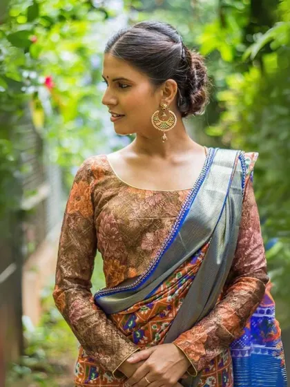 This model wears a printed blouse with long sleeves, accessorized with large, round gold earrings.