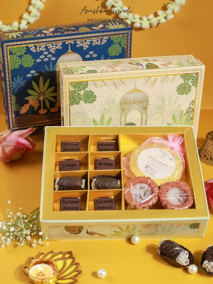 A variation of the peacock-themed Diwali hamper, showcasing different packaging options and contents against a warm yellow background.