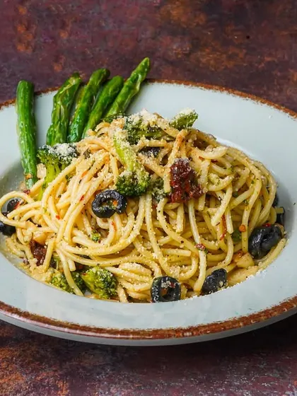 A plate of spaghetti aglio e olio with broccoli and olives, styled with a sophisticated, rustic feel on a dark background.