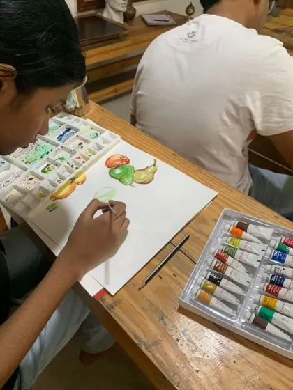 Another angle of students exploring the art of watercolor with still life. You can see the tube paints and palette, essential tools for any watercolor artist.