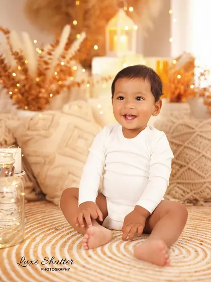 A happy six-month-old baby sitting up on his own in a beautiful, warm-toned boho setup. His smile lights up the entire photo.