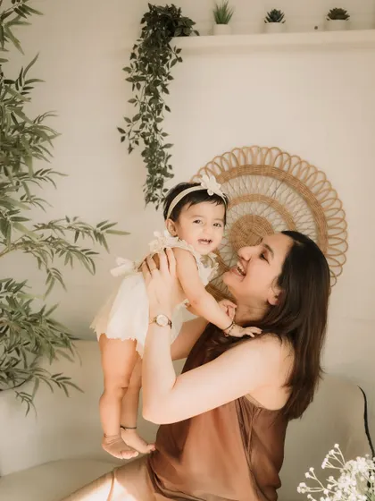 A mother lifts her daughter in the air, both of them beaming with happiness.