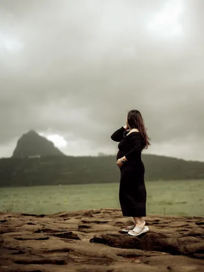 A powerful wide shot of the mom-to-be standing on a rocky outcrop, looking towards the mountains. It’s a portrait of strength and solitude on her motherhood journey.