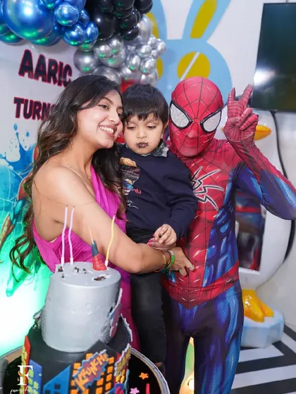 A mother and her son pose with Spider-Man during the cake cutting, a perfect photo opportunity.