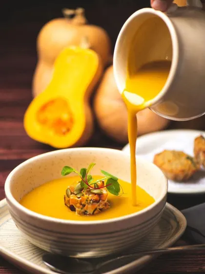 A creamy butternut squash soup being poured, a comforting starter from my Thanksgiving menu.
