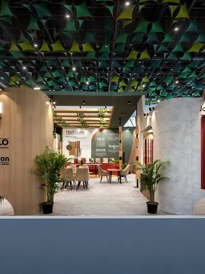 The entrance to the Trustlam pavilion is designed to be open and accessible, with clear branding and a glimpse of the inviting interior. The design uses a mix of wood, concrete textures, and greenery to reflect a modern yet earthy brand identity.