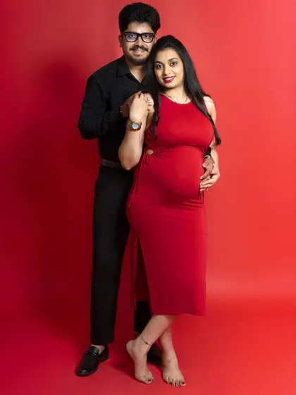 A classic, happy portrait of an expectant couple against a bright red background. Their smiles show the pure joy and excitement of waiting to become parents.