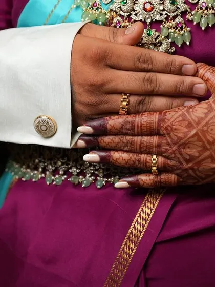 A close-up shot focusing on the couple's hands and rings during their engagement. The bride's mehendi, with its classic check pattern, adds to the beauty of the moment.