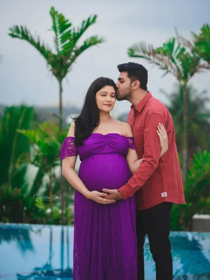 A tender moment captured as a partner kisses his pregnant wife's forehead during their poolside maternity shoot. The purple gown adds a touch of royalty.