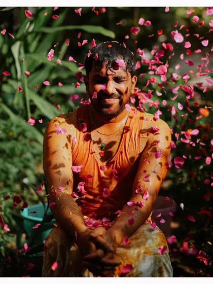The groom sits with his eyes closed as he is showered with pink rose petals during his Haldi.