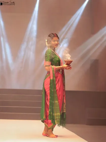 A side profile of the model from the NAVATAAR show, giving a different perspective on the outfit and the prop. This angle captures her serene expression under the dramatic stage lights.