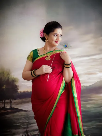 A graceful portrait in traditional attire. The mom-to-be, in a red and green saree, holds a peacock feather, her pose elegant and timeless.