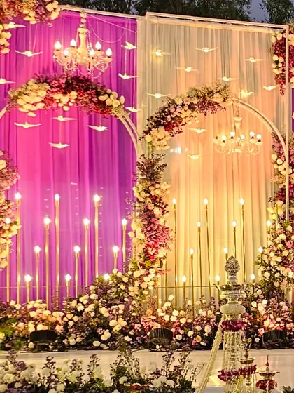 We created a paradise-like setting with layered floral arches, elegant chandeliers, and warm candle lighting. The combination of pink and white drapes with abundant flowers results in a truly dreamy and romantic stage.