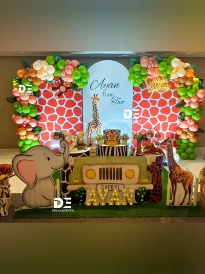 Welcome to Ayan's safari! This setup for a second birthday features a jeep-shaped main table, friendly animal cutouts like a large elephant and tiger, and a giraffe-print backdrop framed by a beautiful organic balloon garland.