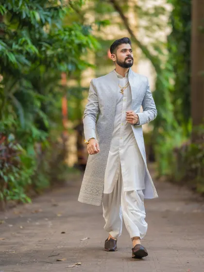A stylish portrait of the groom in his reception attire, a modern sherwani, captured in a natural outdoor setting.