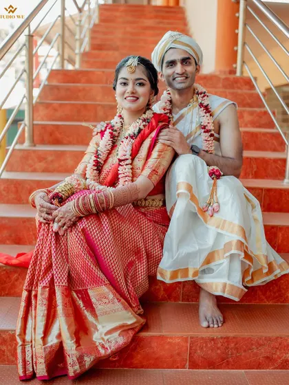 A happy and relaxed portrait of the couple sitting on bright orange steps, their traditional attire contrasting beautifully with the modern setting.