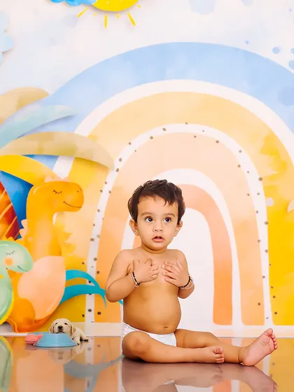 A curious expression from a baby boy in a diaper, set against a colorful dinosaur and rainbow background. This is a simple, sweet shot from a themed sitter session.