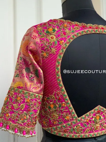 A beautiful example of a mixed-media back design. This pink blouse features a large circular cutout framed with vibrant, multi-colored floral embroidery that contrasts with the brocade sleeves.