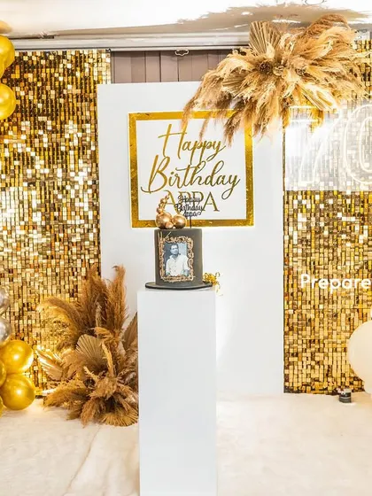 A grand 70th birthday celebration with a gold and white theme. This setup includes a gold sequin wall, a personalized backdrop, and an elegant balloon garland with pampas grass accents.