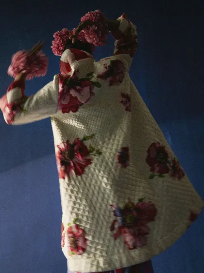 This image showcases the back of a reversible floral jacket, styled with a dramatic floral headpiece. The pose and dark, moody lighting create a sense of mystery and highlight the garment's unique, artistic details.