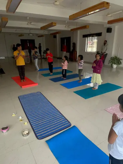 A regular weekly class in session. Children learn the foundations of yoga, including standing poses and prayer, in a group setting that fosters mutual respect and shared learning.