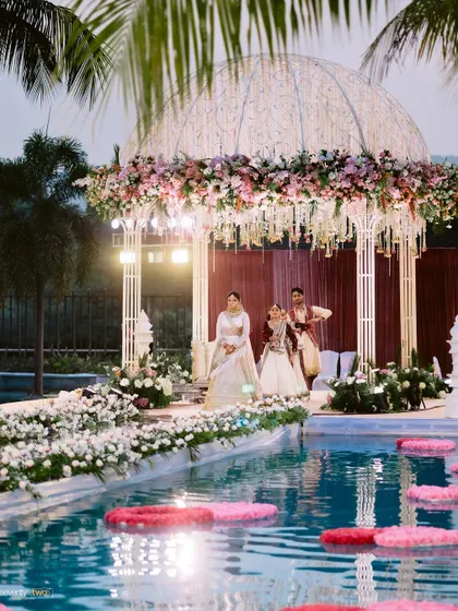 The bride and groom make their entrance onto the poolside mandap at their Karjat wedding, a truly grand and unique setting for their vows.