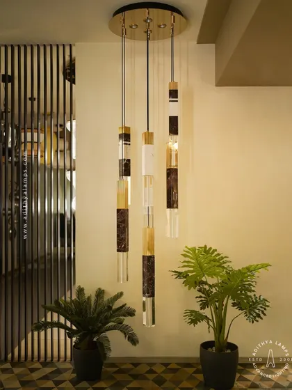 This cluster of pendant lights showcases a luxurious blend of materials, combining solid marble, fluted gold metal, and clear crystal. Suspended at varying heights, they create a dynamic and elegant focal point, ideal for stairwells or entryways.