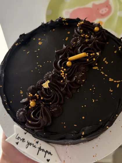 A rich, dark chocolate mini cake with elegant piping and a sprinkle of gold dust. A simple and decadent treat.