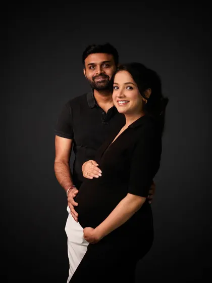 A happy and classic studio portrait of the couple looking towards the camera, ready to welcome their new addition.