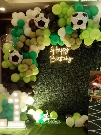 A close-up of the left side of the football backdrop, highlighting the neon 'Happy Birthday' sign, the marquee number '11', and the detailed balloon arch with mini soccer ball accents.