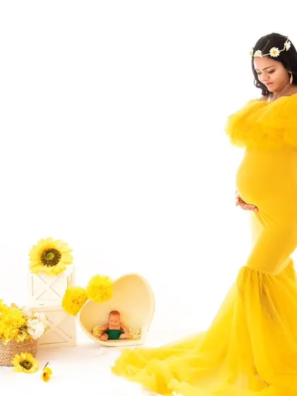 Another pose from the sunny yellow gown session. The mom-to-be stands, holding her bump, offering a full-length view of the beautiful gown and the bright, cheerful studio setup.