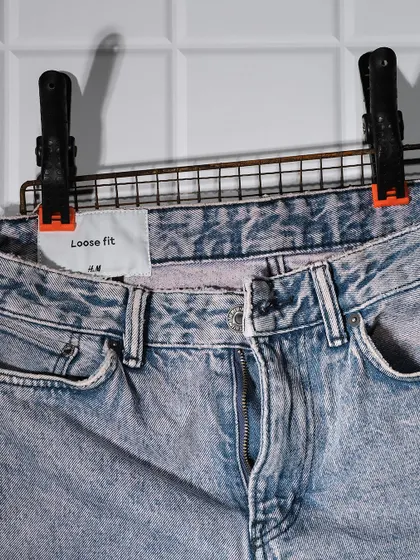 A detailed shot of H&M loose-fit jeans, focusing on the acid-wash texture and waist details. Close-ups like this are crucial for customers to assess fabric and quality online.