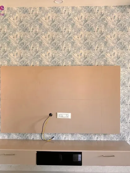 A living room accent wall featuring a delicate, nature-inspired wallpaper. We paired this with a neutral paint color on the adjacent walls and TV unit to create a balanced and harmonious design.