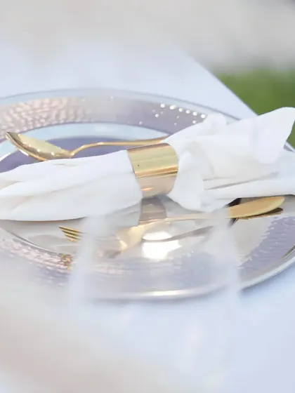 An elegant table setting featuring a hammered silver charger plate and gold-accented cutlery. We believe luxury is in the details, and our sophisticated place settings elevate the dining experience for every guest.