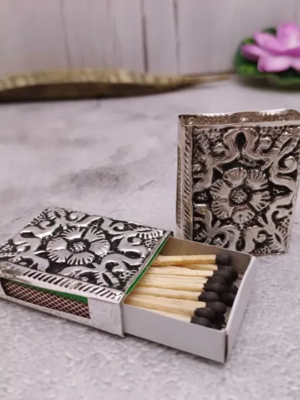 A beautifully carved German silver matchbox cover. It's a small detail that adds a lot of elegance to your pooja setup.