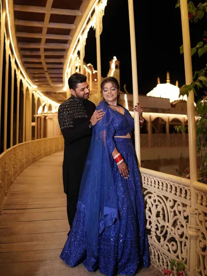 A romantic nighttime portrait of the couple on an illuminated bridge at Lohagarh Fort, the royal blue of the bride's lehenga creating a stunning contrast.