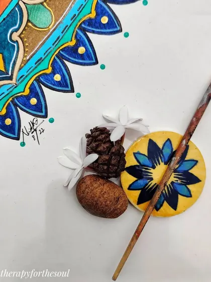 Another detail shot of the 'Peacock in the Desert Rain' mandala, with a brush and a small painted stone, hinting at the creative process.