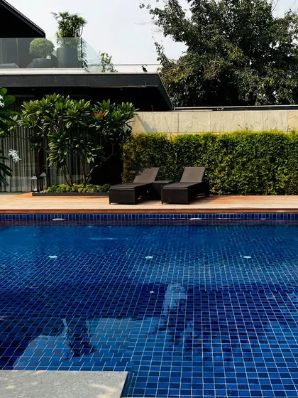 Another view of the poolside at the Sultanpur farmhouse project. The deep blue mosaic tiles of the pool contrast beautifully with the warm wood of the deck and the vibrant green of the surrounding privacy hedge.