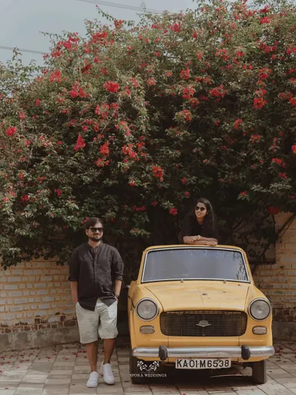 The couple posing with a vintage car under a vibrant bougainvillea tree, a picture of retro romance.