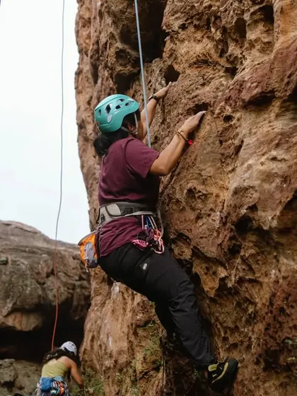 A participant on a top-rope climb in Badami, fully equipped with a helmet and harness. Safety is our top priority, allowing beginners to confidently experience the thrill of height.