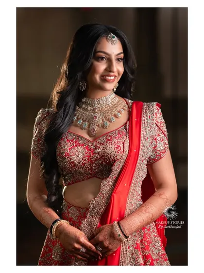 A beautiful portrait of Likitha for her reception. Her makeup features a soft, glowing base and a warm, glossy lip, perfectly complementing her traditional red lehenga and diamond jewelry.