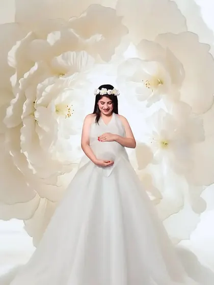 An angelic vision in white. This portrait features a beautiful white gown with a floral headpiece, set against a giant white flower prop to create a soft, ethereal, and heavenly atmosphere.