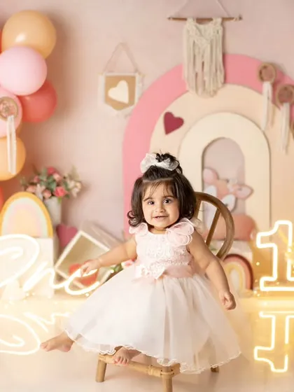 A pretty princess in a beautiful dress, sitting on a tiny chair in her colorful first birthday setup.