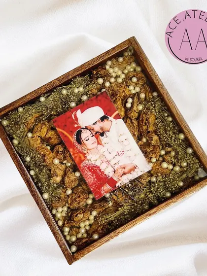 Your wedding photo and varmala, together forever. This square teakwood frame holds a couple's picture surrounded by their preserved wedding flowers and delicate pearls, capturing the essence of their day.