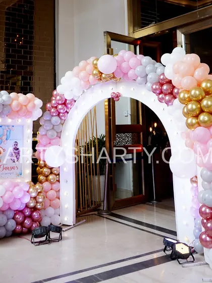 A stunning entrance arch in shades of pink, rose gold, and white, with a personalized welcome sign for a glamorous teddy bear party.