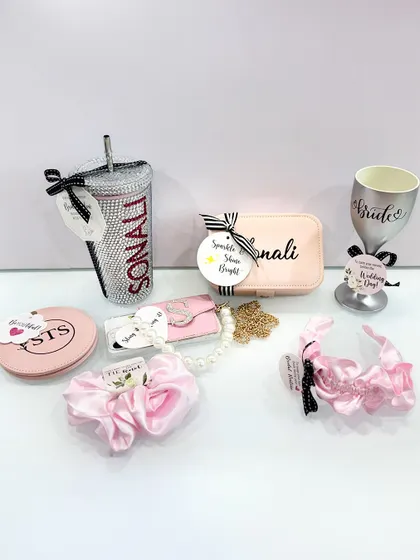 A collection of personalized accessories for the bride, including a blinged-out tumbler, a custom wine glass, and various pouches and scrunchies.